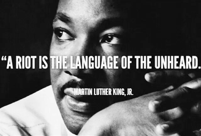 The meme is a black-and-white image of Martin Luther King Jr. with a quote superimposed over his face. The quote is in a bold, white font and reads: "A riot is the language of the unheard."